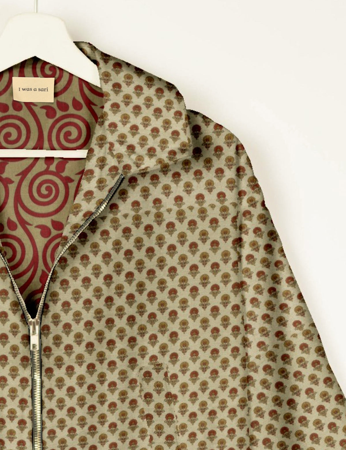 Beige bomber jacket with small floral print, front zipper, and red swirl patterned lining labeled "I was a sari" on hanger