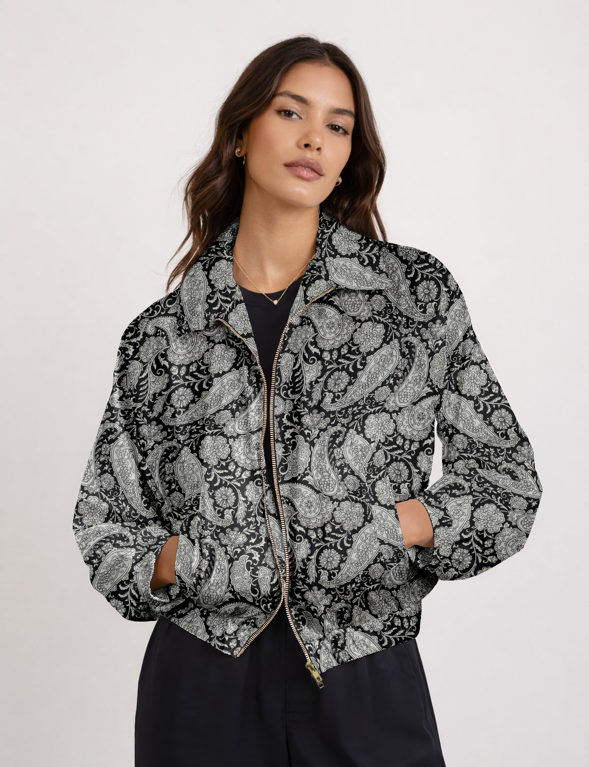 Woman wearing a black bomber jacket with gray paisley and floral pattern, front zipper, and side pockets, front view