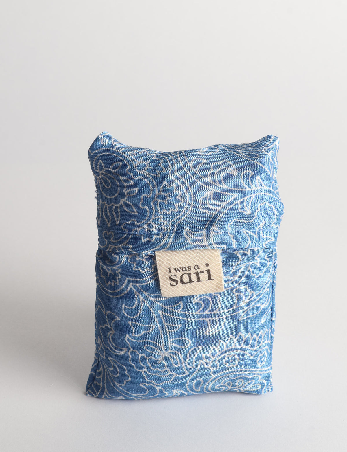 Blue reusable bag with white floral paisley pattern folded with a beige label reading "I was a sari" on front