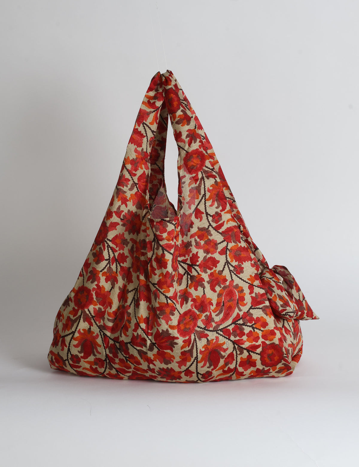 Blue reusable bag with tropical floral pattern in pink, yellow, and green, shown hanging with handles visible