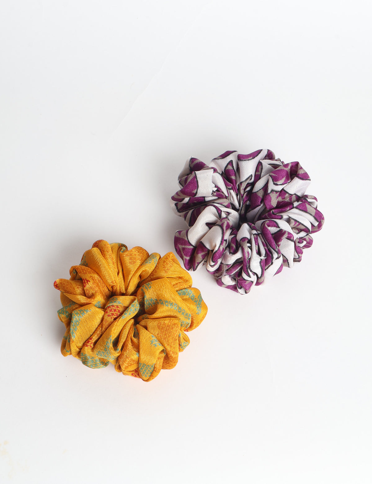 Set of two fabric scrunchies, one turquoise with beige abstract spots, one red with white linear pattern, flat lay on white