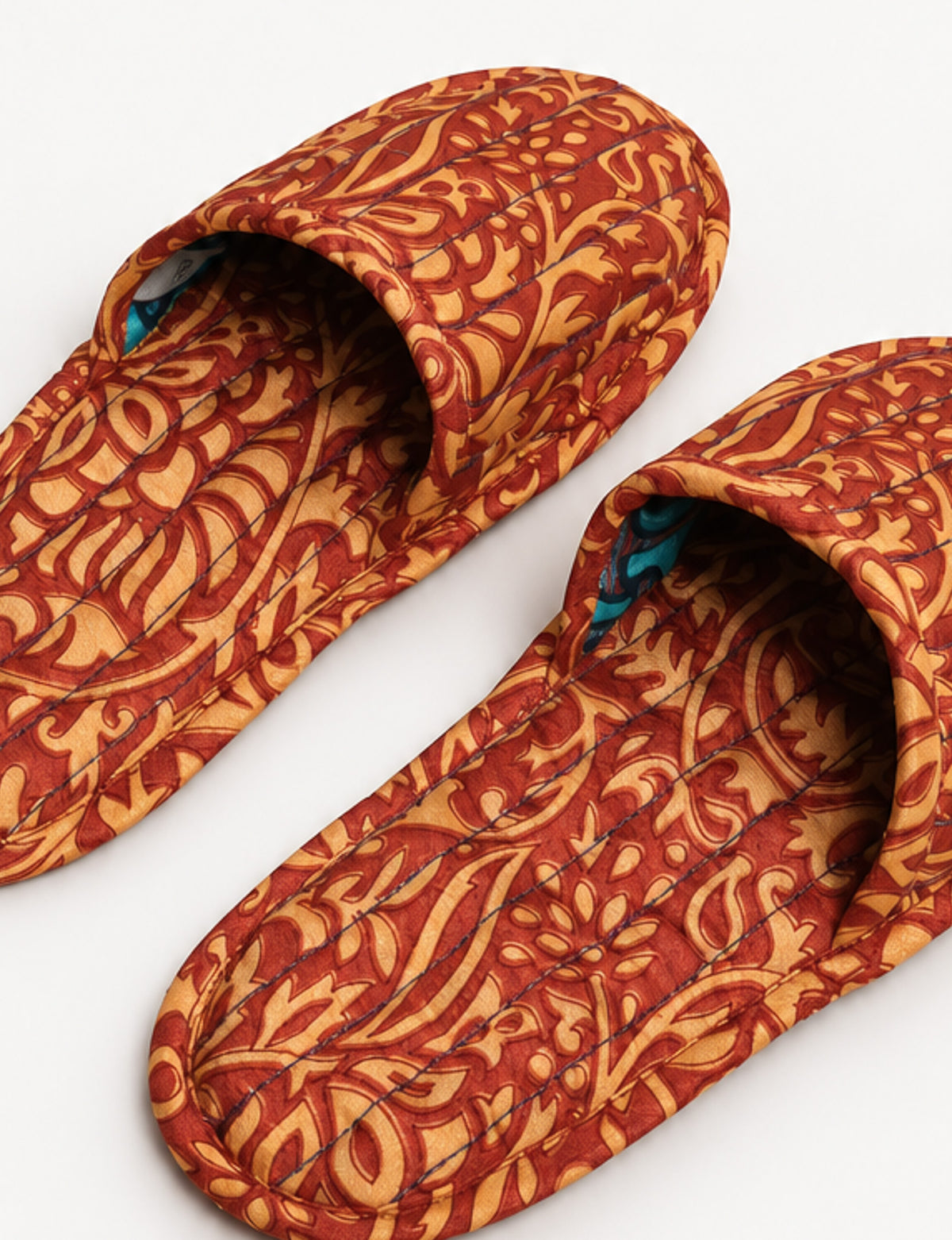Blue quilted slippers with paisley pattern in shades of purple, green, and pink, shown from top view on white background