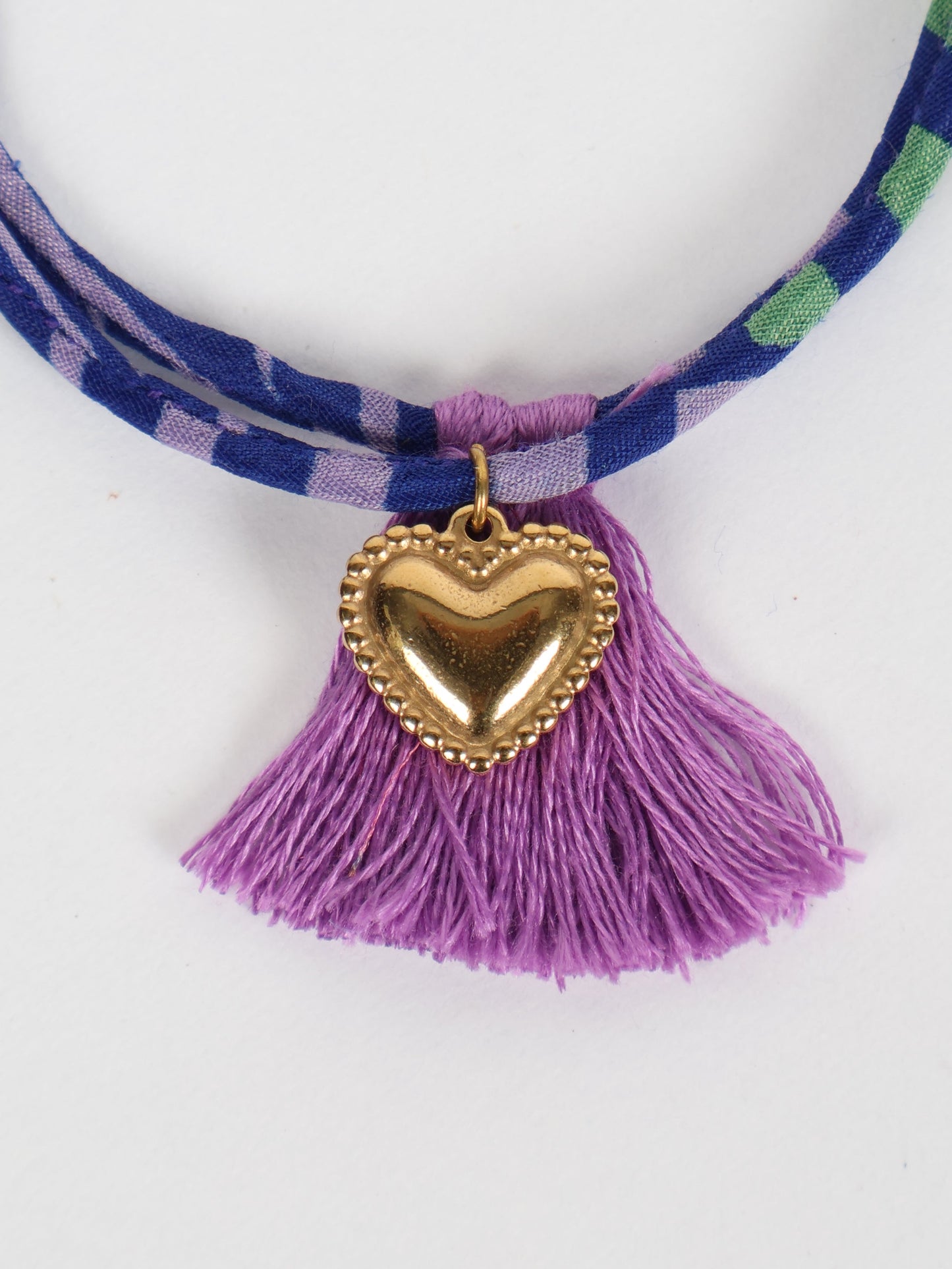 Handmade rope bracelet from recycled sari fabric with gold heart charm and tassels—eco friendly cloth, climate neutral fashion, and upcycled women’s clothing.
