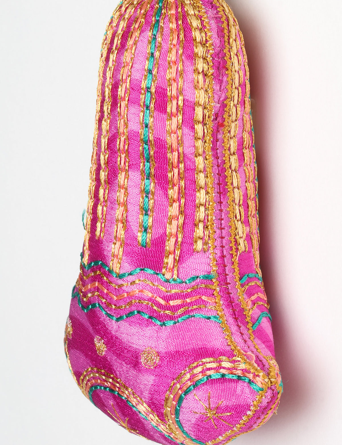 Close-up of a pink fabric bell ornament with gold, teal, and peach embroidered vertical stripes and floral patterns