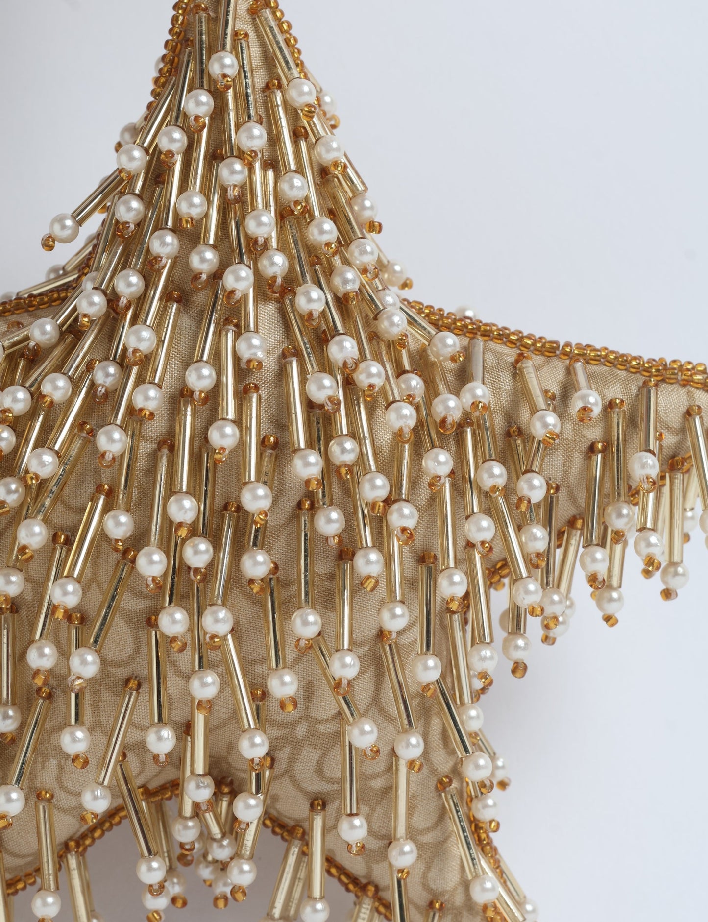 Gold colored star ornament made from ivory and gold preloved saris, filled with organic cotton and decorated with silver hand embroidery, representing upcycled clothing, green fashion, fair trade fashion, recycled material clothing, repurposed clothing, climate neutral clothing, eco clothing, second hand clothing, recycled sustainable fashion, and sustainable women’s clothing.