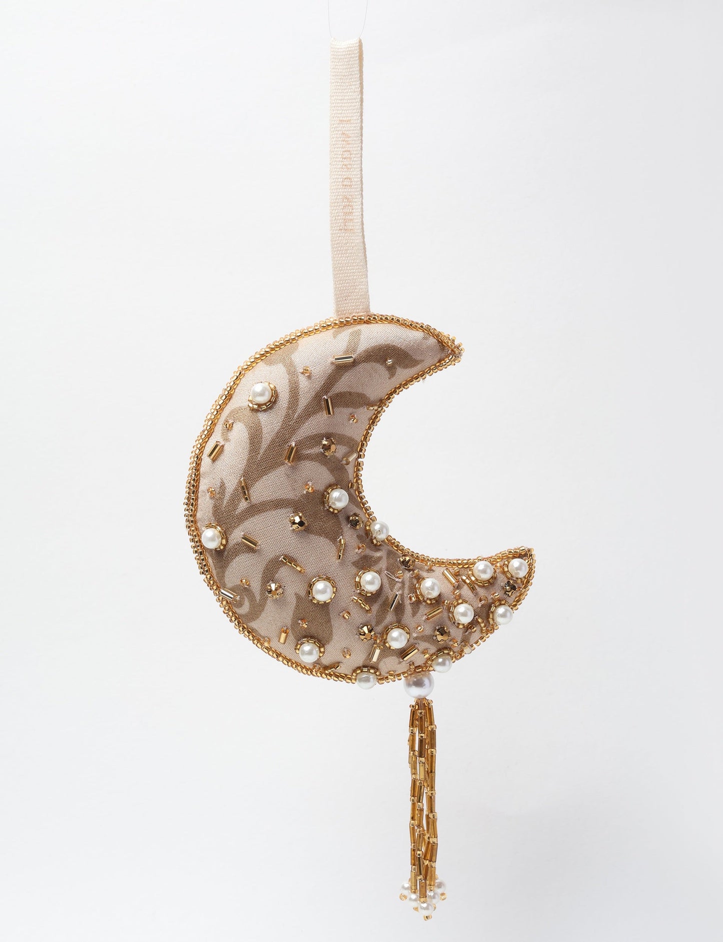 A crescent moon ornament made from ivory and cream recycled fabric, filled with organic cotton, embellished with gold stones and beads. This recycled clothing piece aligns with circular fashion, earth friendly clothing, and fashion revolution ideals, crafted to support repurposed clothing and eco friendly fashion.