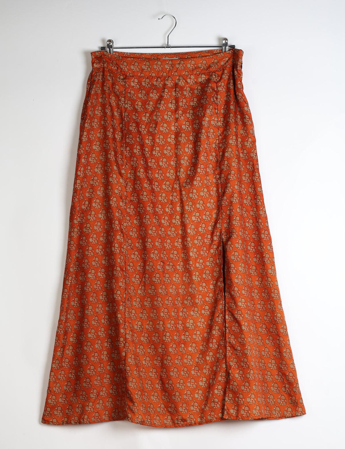 Orange A-line skirt with small floral pattern and side slit, hanging on a metal hanger against a white background