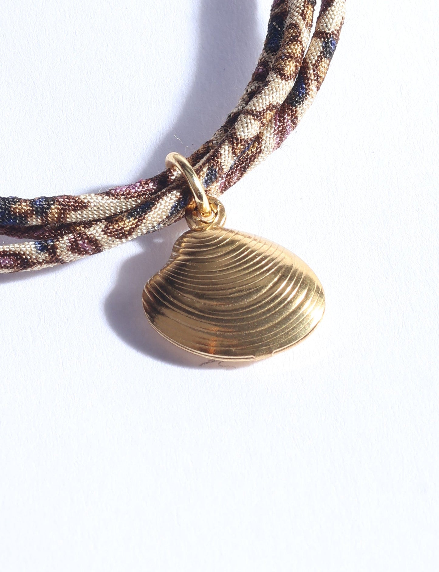 Adjustable slim cord bracelet with gold-plated stainless steel shell charm inspired by upcycled women’s clothing, sustainable women’s clothing, eco friendly clothes, recycled sustainable fashion, carbon neutral clothing, and environment friendly clothing values.