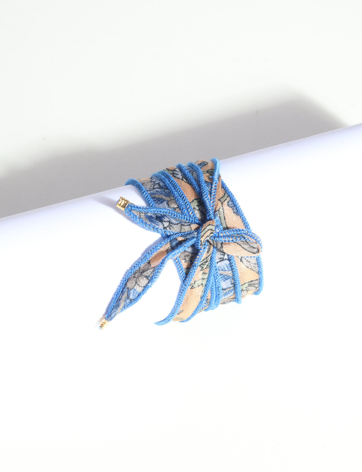 Wrap-around bracelet with blue-edged orange and blue abstract patterned fabric tied in a bow on white background
