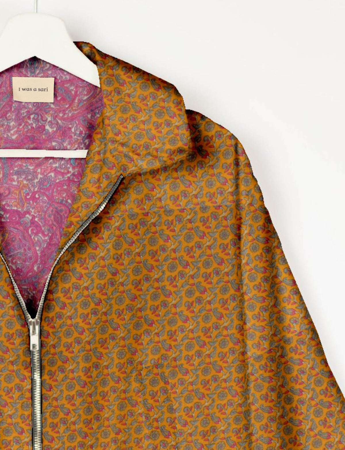 Yellow bomber jacket with tropical floral pattern, silver zipper, and pink paisley inner lining on white hanger