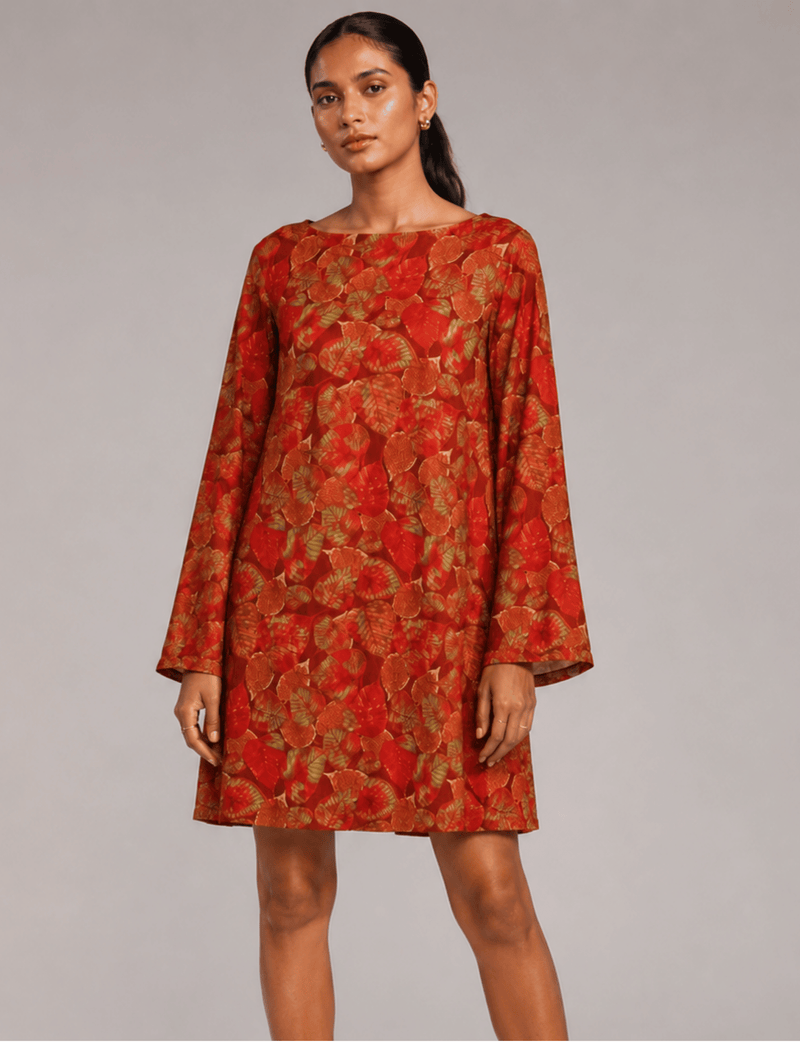 Model wearing a red swing dress with an all-over red and green leaf pattern, long sleeves, and a round neckline