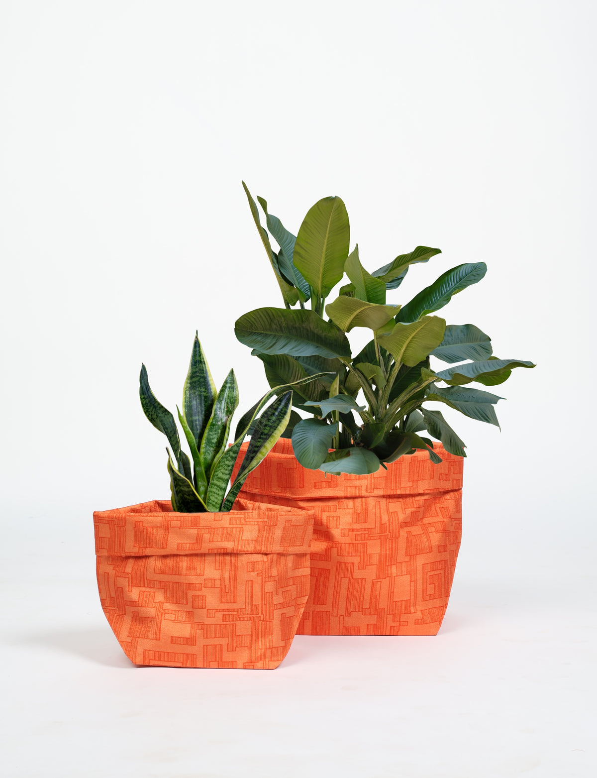Set of two orange fabric plant pot covers with abstract geometric patterns, holding green leafy plants, front view