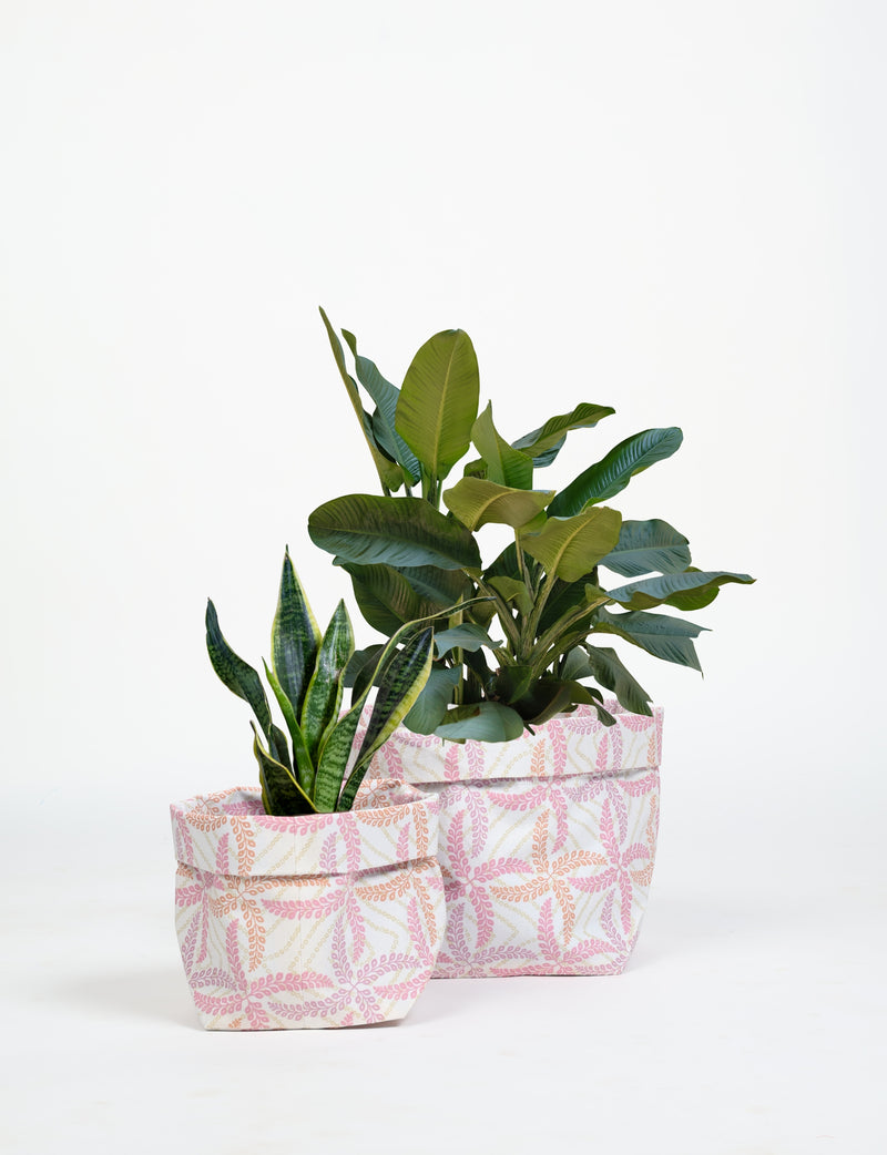 Two fabric plant pot covers in white with pink and orange leaf patterns, holding green leafy plants, front view
