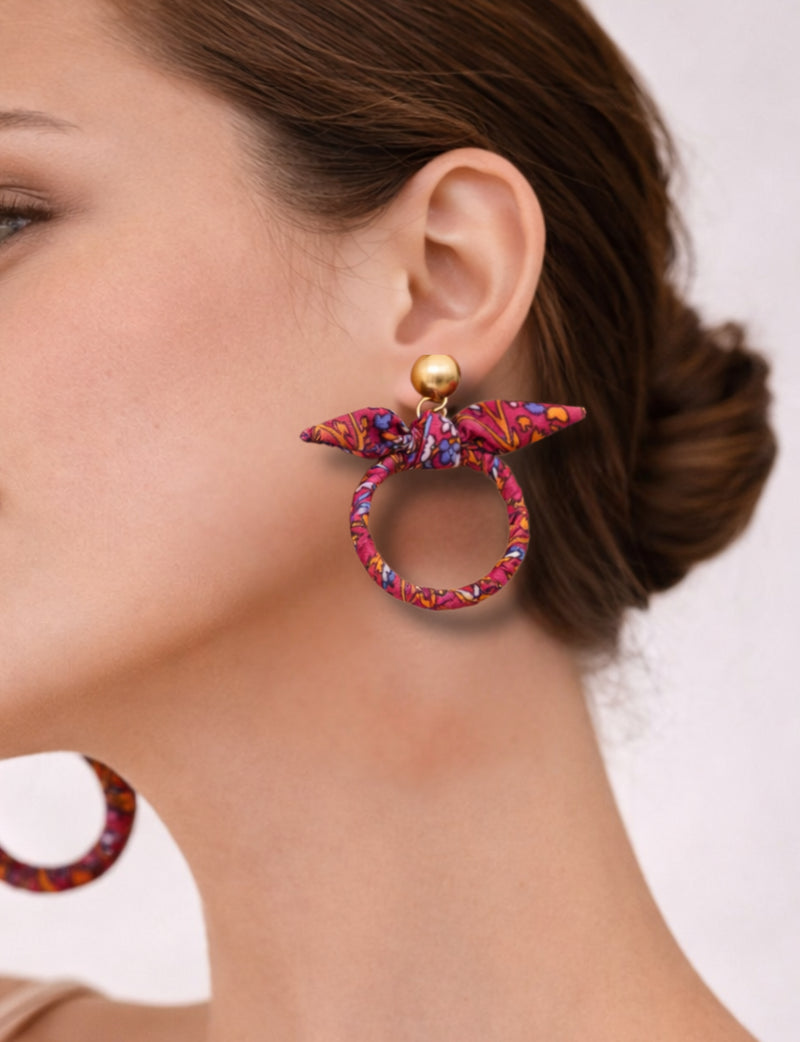 Pink tropical fabric bow earrings with gold round stud, worn by model showing side profile and brown hair updo