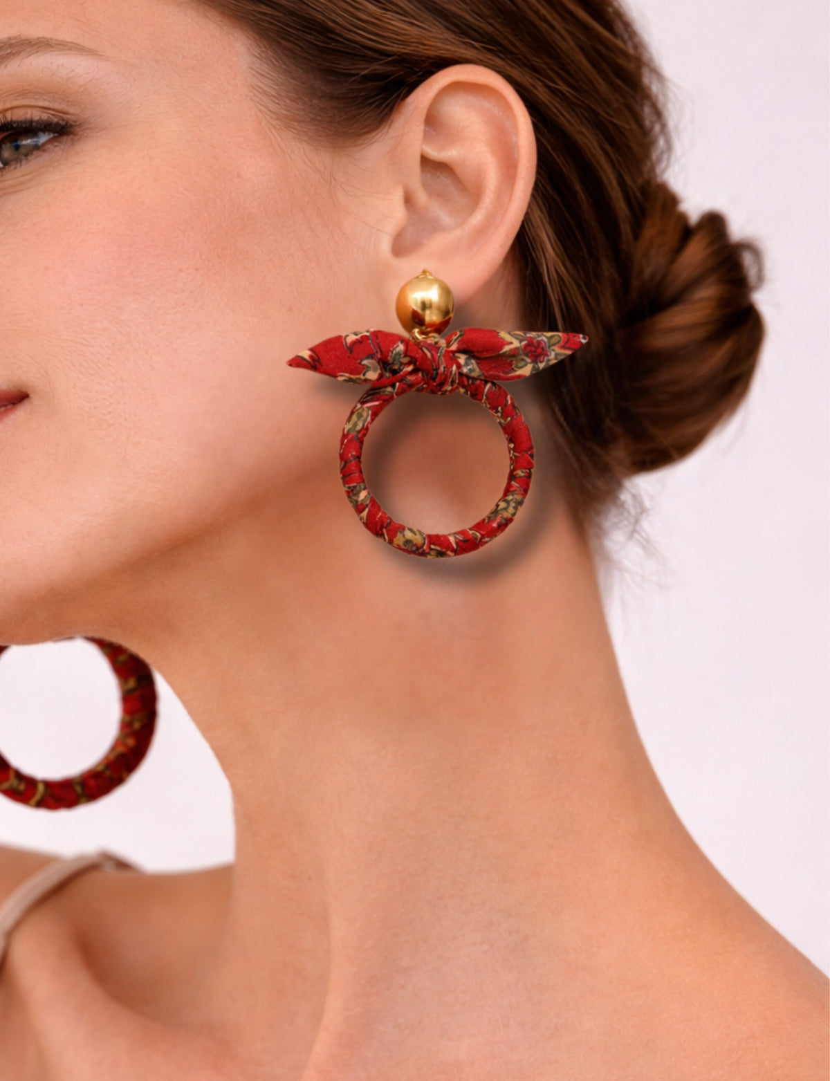 Red tropical fabric bow earrings with gold round stud, worn by model showing side profile and neck