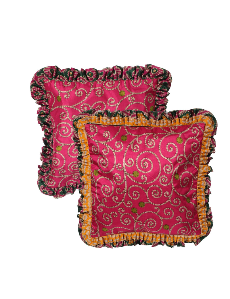 Set of two red cushion covers with abstract swirl patterns and double frill edges in green and orange, flat lay view