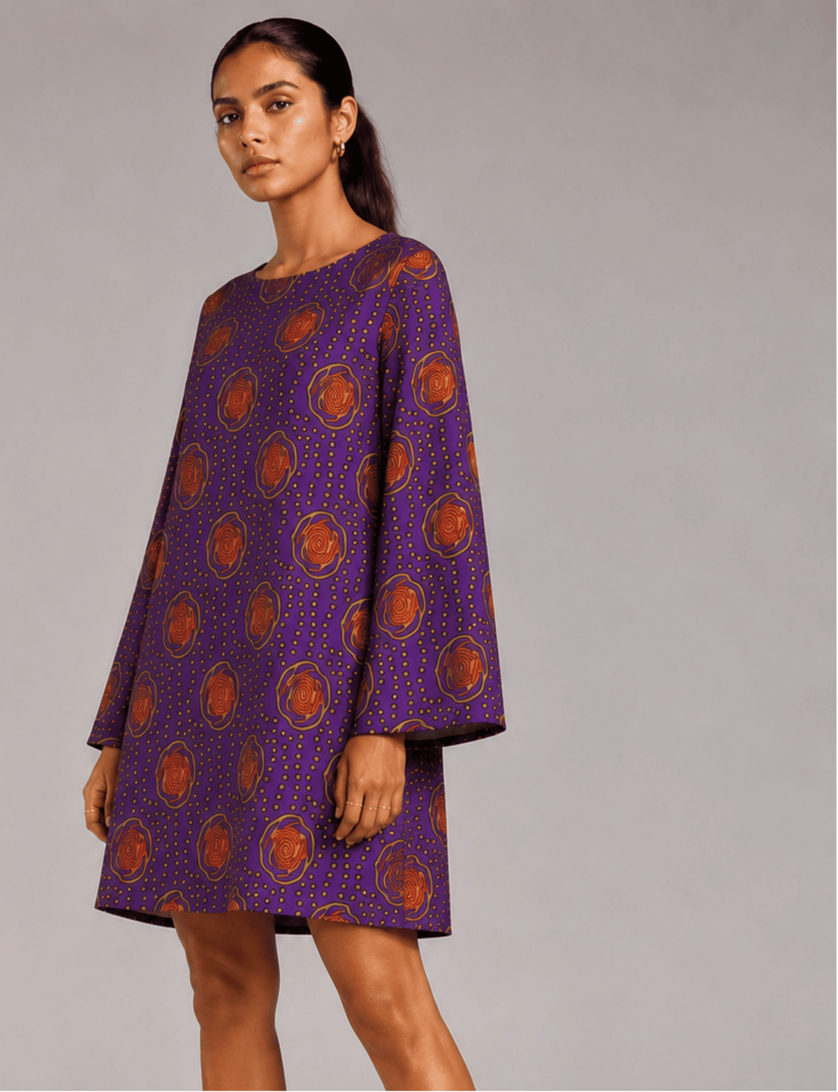 Model wearing a purple swing dress with orange floral and dotted pattern, long sleeves, and a round neckline, front view