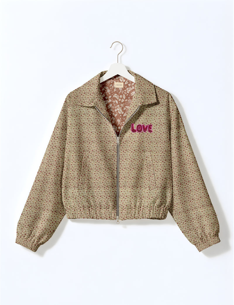 Beige floral bomber jacket with front zipper, elastic cuffs, collar, and pink "LOVE" embroidery on chest, shown on white hanger