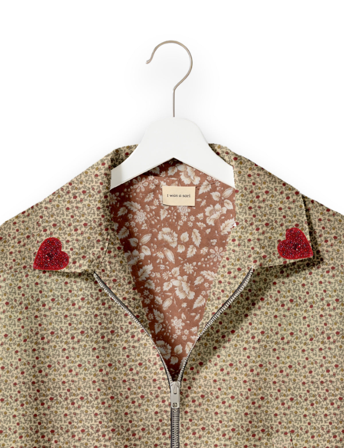 Beige floral bomber jacket with red beaded heart patches on collar, front zipper, and floral inner lining, on white hanger