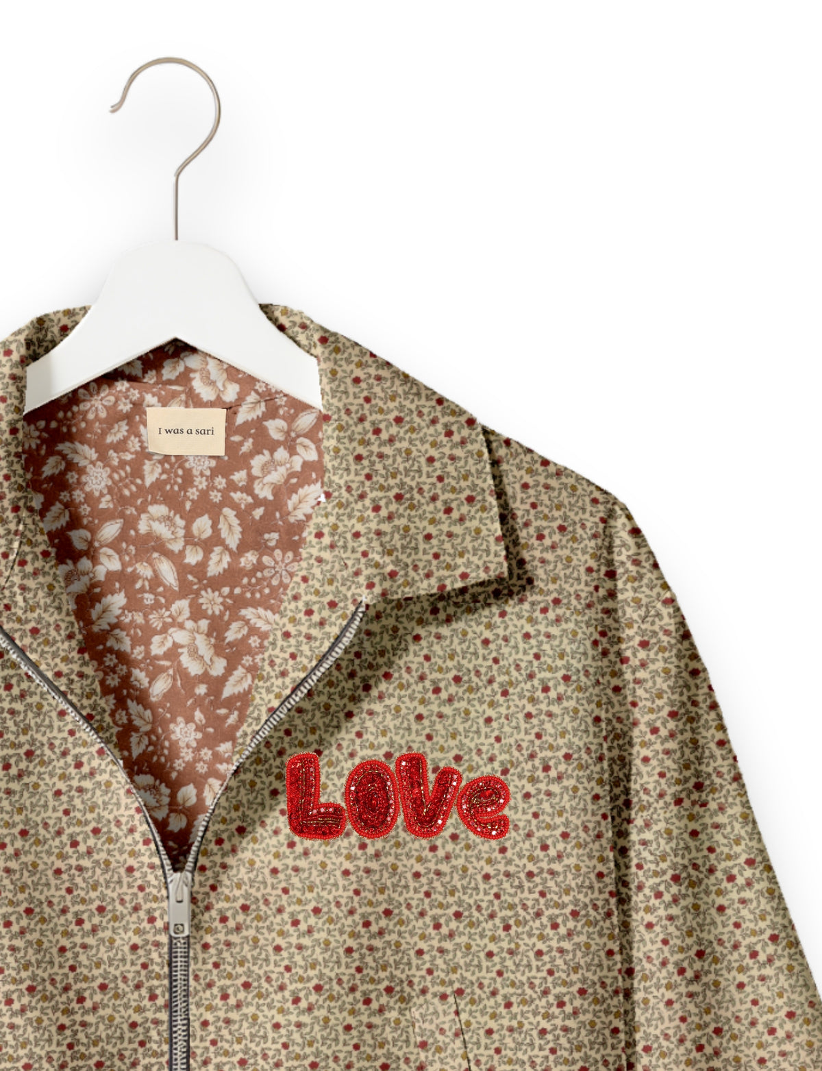 Beige floral bomber jacket with red sequined "LOVE" patch, front zipper, and contrasting floral inner lining on white hanger
