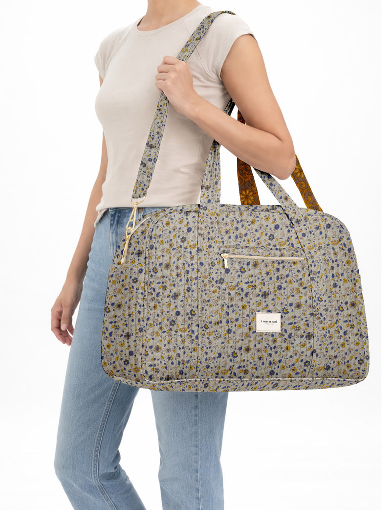 Brown quilted duffle bag with paisley pattern, front zip pocket, dual handles, and label reading "I was a sari"