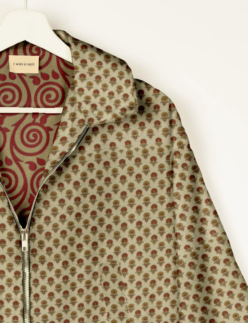 Beige bomber jacket with small floral print, front zipper, and red swirl patterned lining labeled "I was a sari" on hanger