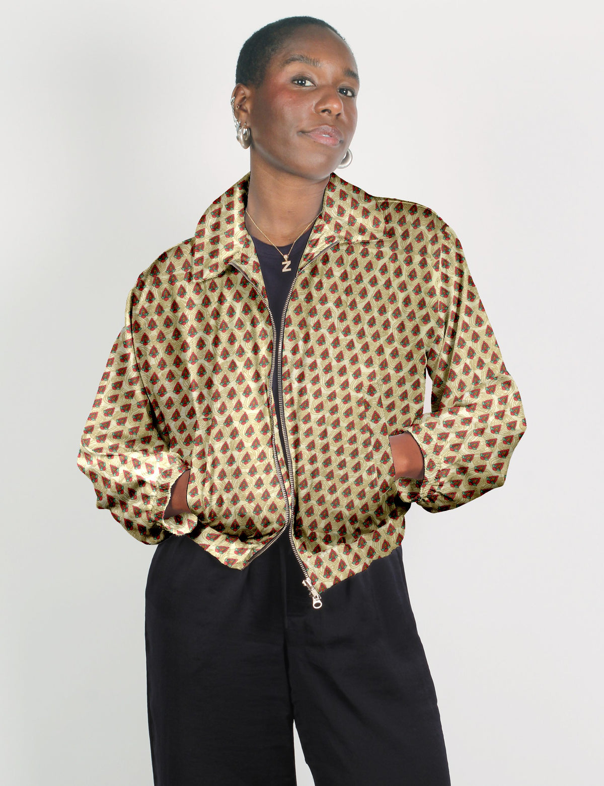 Woman wearing beige bomber jacket with red and green Indian ethnic pattern, front zipper, and elastic cuffs, paired with