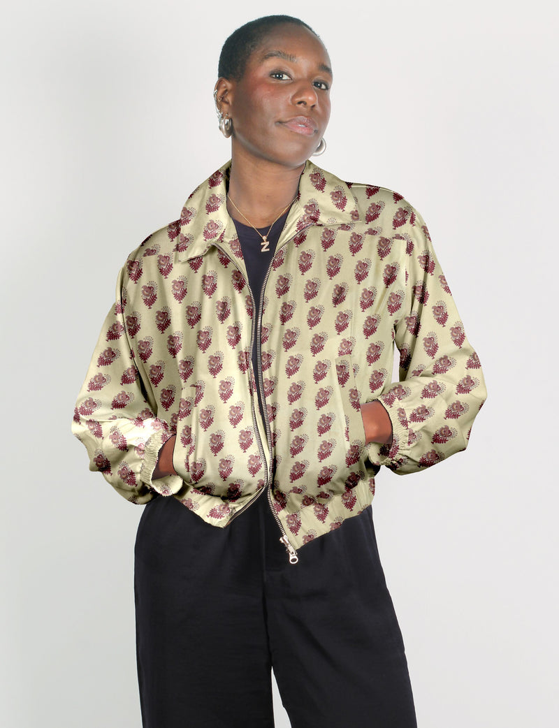 Woman wearing beige bomber jacket with maroon leaf pattern, front zipper, elastic cuffs, and collar, paired with black pants