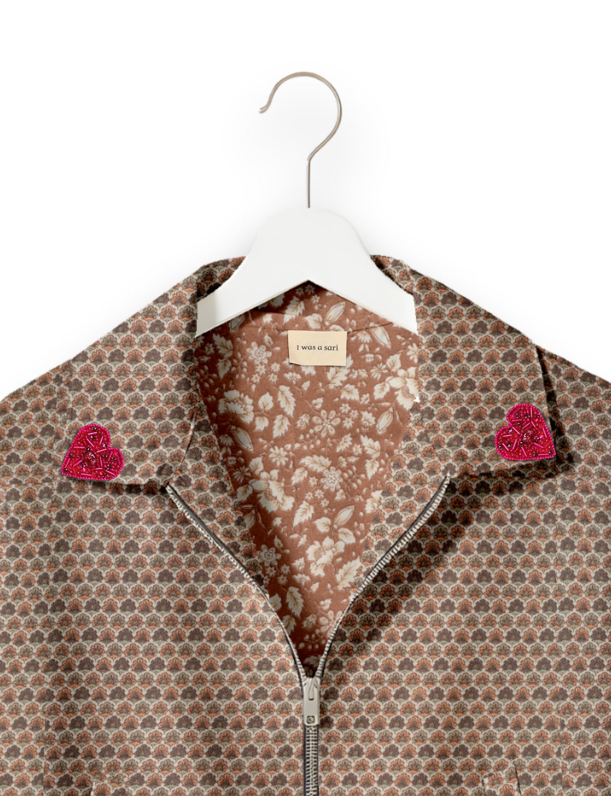 Beige bomber jacket with micro floral pattern, pink beaded heart patches on collar, and silver zipper, hanging on white hanger