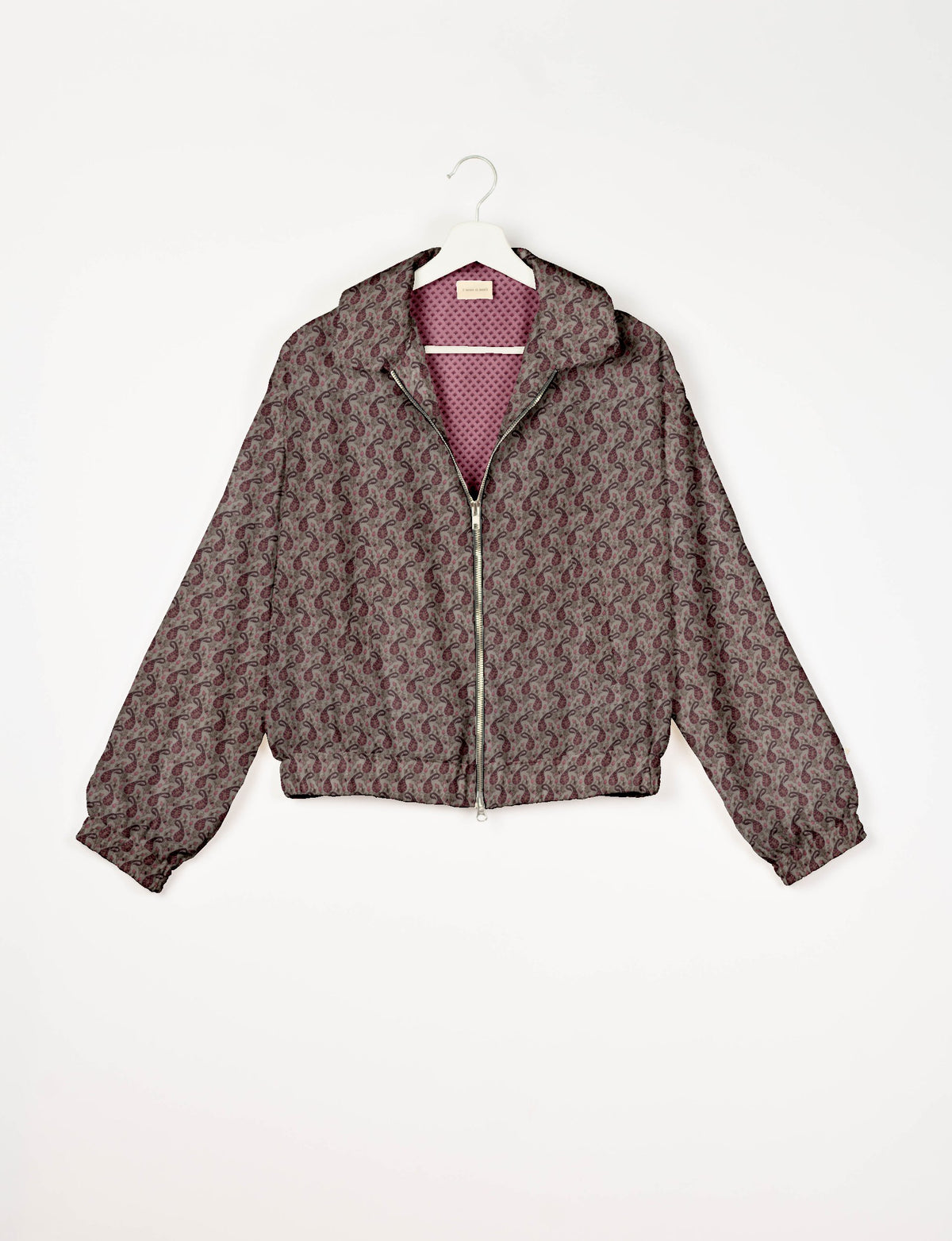 Beige bomber jacket with maroon paisley pattern, front zipper, elastic cuffs, and pink textured inner lining, hanging on