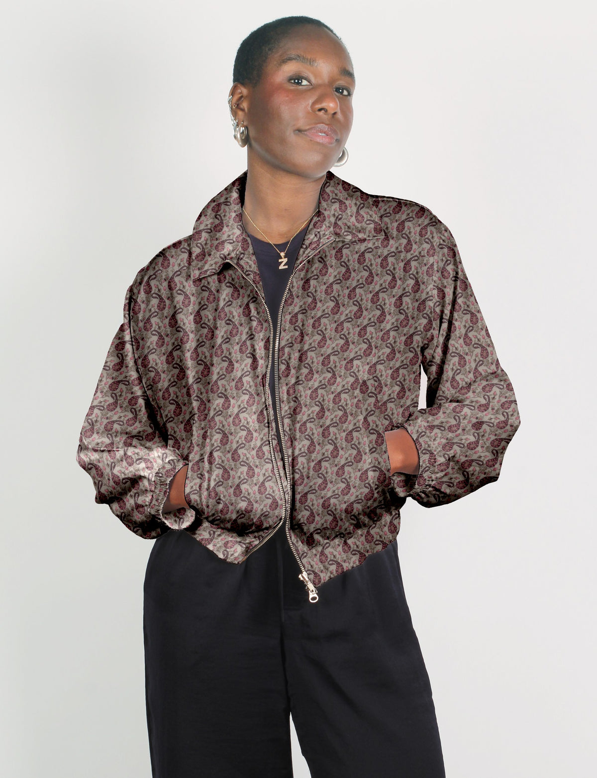 Woman wearing beige bomber jacket with maroon paisley pattern, front zipper, elastic cuffs, and collar, paired with black