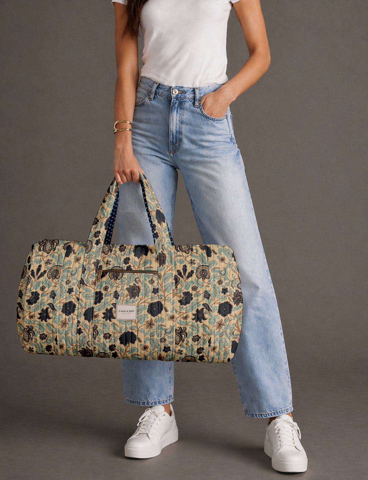 Quilted brown paisley barrel bag with double handles, front pocket, and gold zipper, shown in side angle view