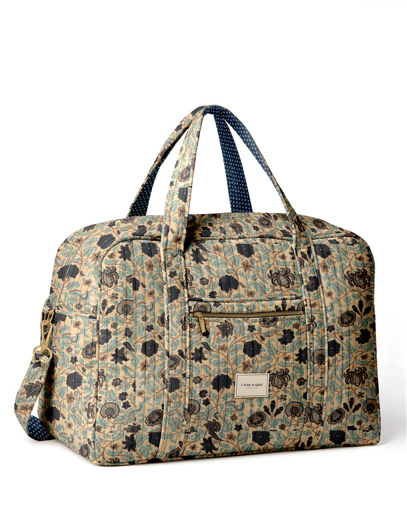 Brown quilted duffle bag with paisley pattern, front zip pocket, dual handles, and label reading "I was a sari"