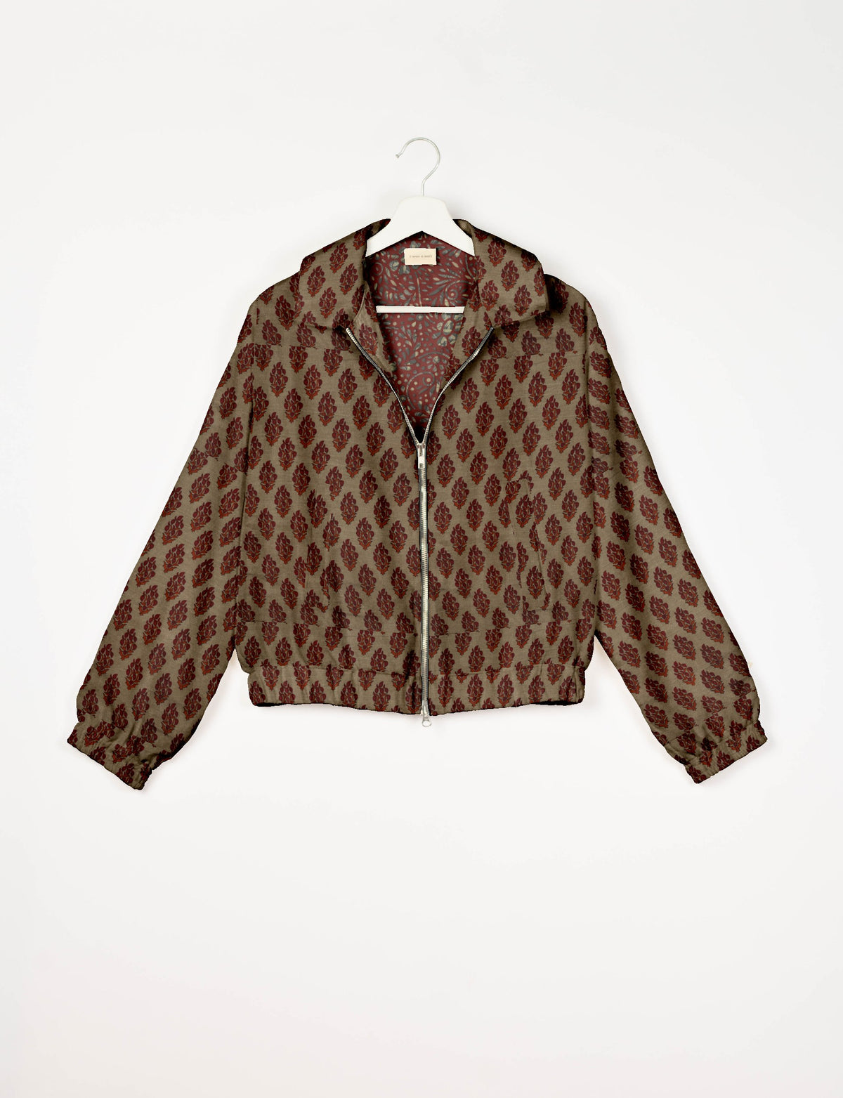 Beige bomber jacket with red tropical leaf pattern, front zipper, elastic cuffs, and collar, hanging on white hanger