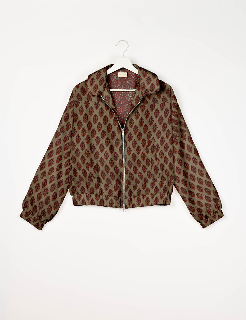 Beige bomber jacket with red tropical leaf pattern, front zipper, elastic cuffs, and collar, hanging on white hanger