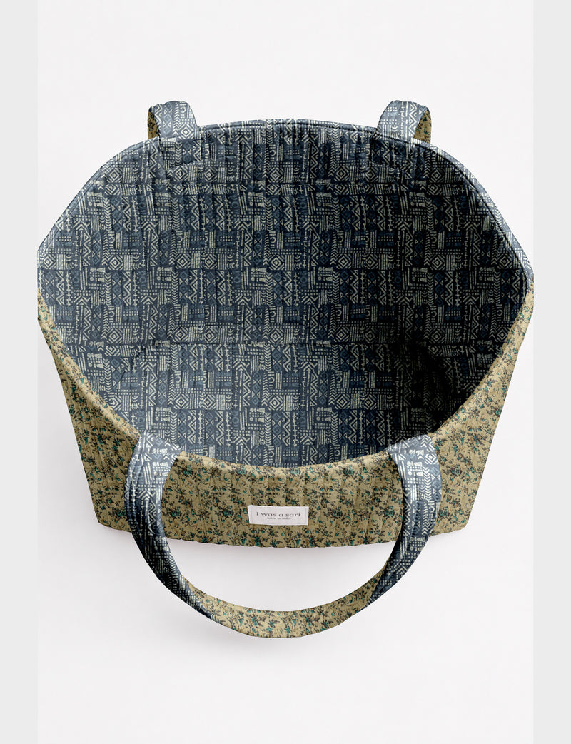 Quilted beach bag with yellow tropical exterior and red patterned interior, shown from top view with handles visible