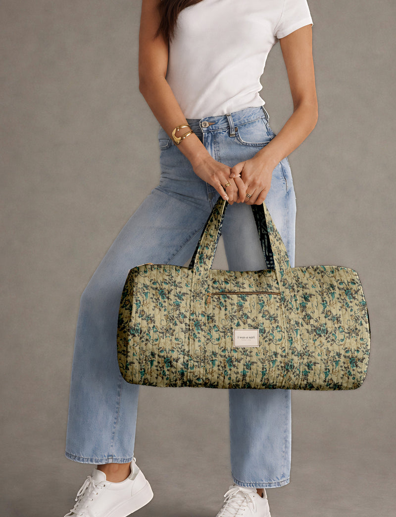 Brown paisley quilted bowling bag with front zipper pocket, held by person wearing white shirt and light blue jeans