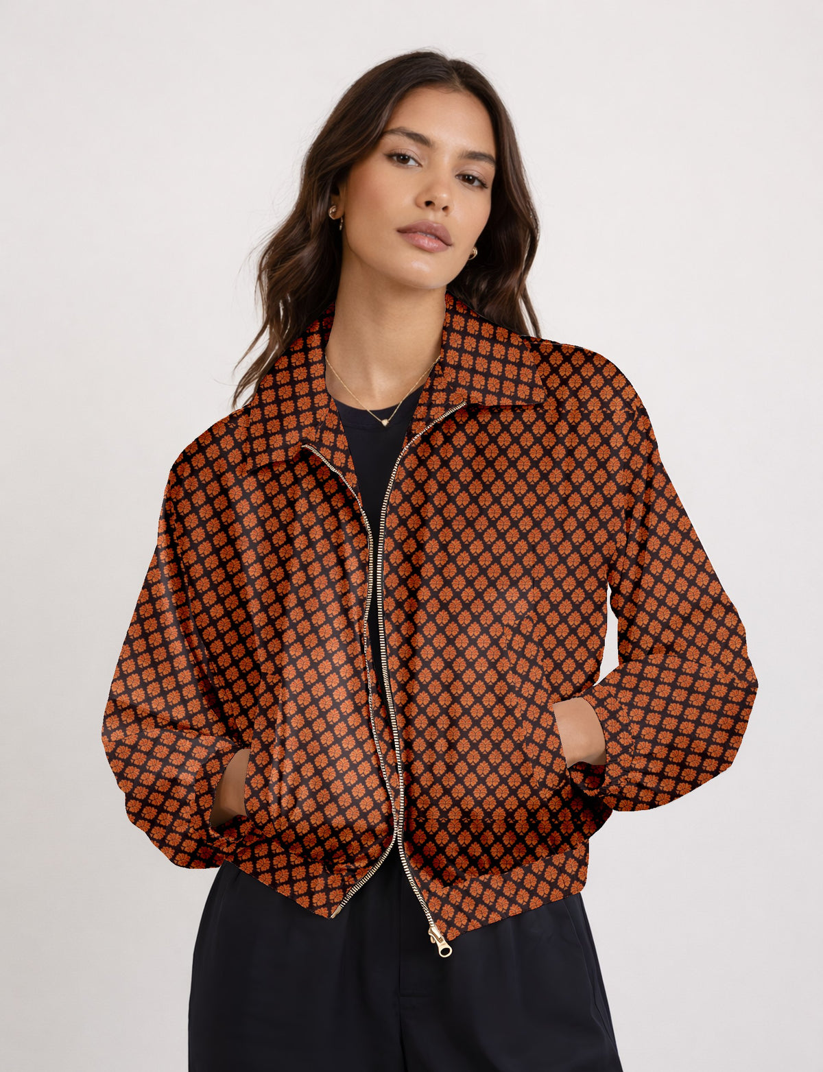 Woman wearing a black bomber jacket with an orange leaf pattern, front zipper, and side pockets, shown from front view
