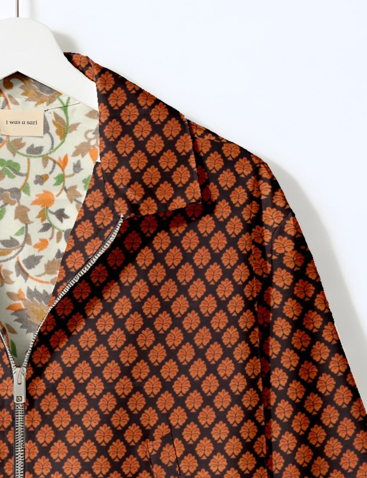 Black bomber jacket with orange leaf pattern, silver zipper, and floral patterned inner lining on white hanger