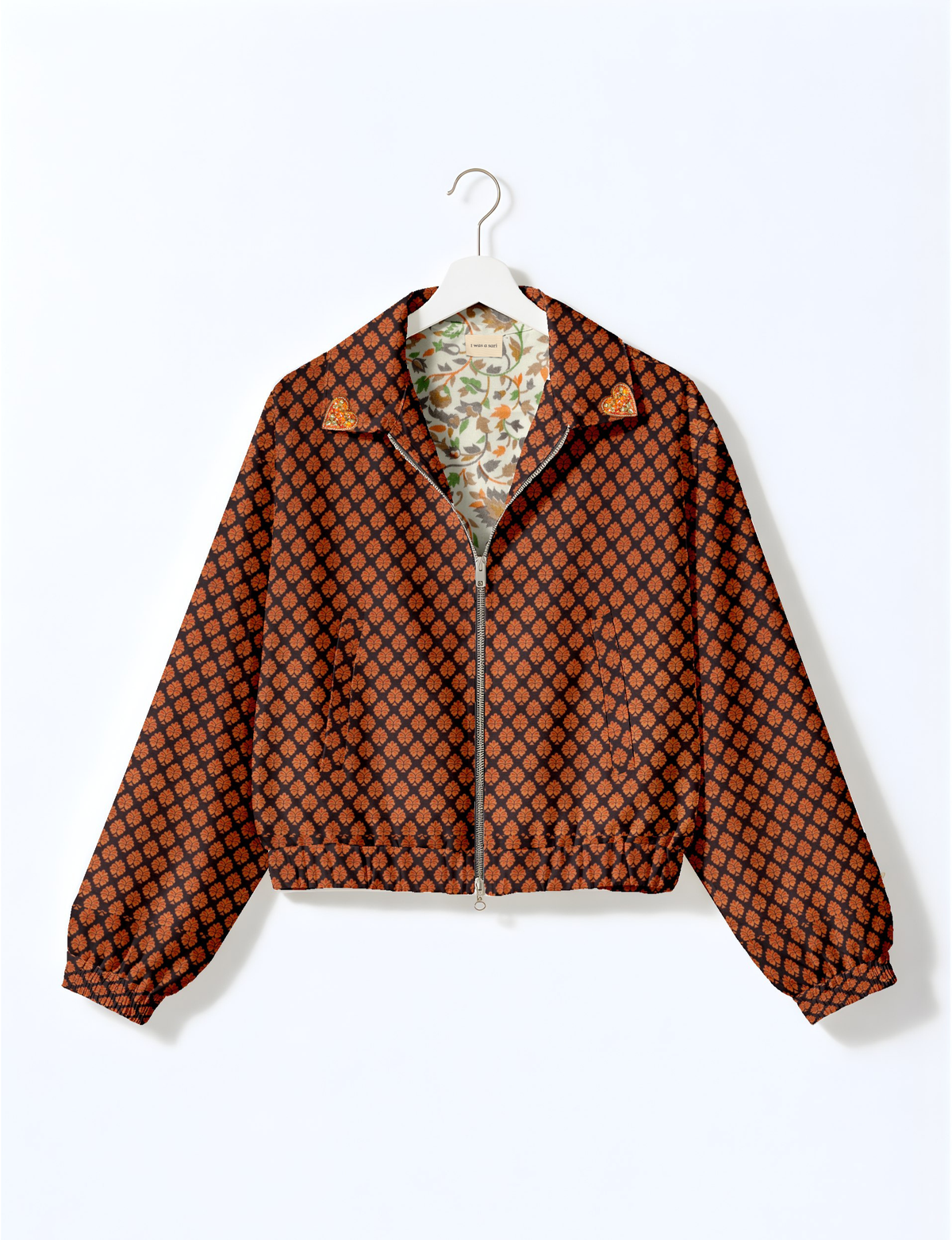 Black bomber jacket with orange leaf pattern, front zipper, elastic cuffs and hem, and gold heart patches on collar tips