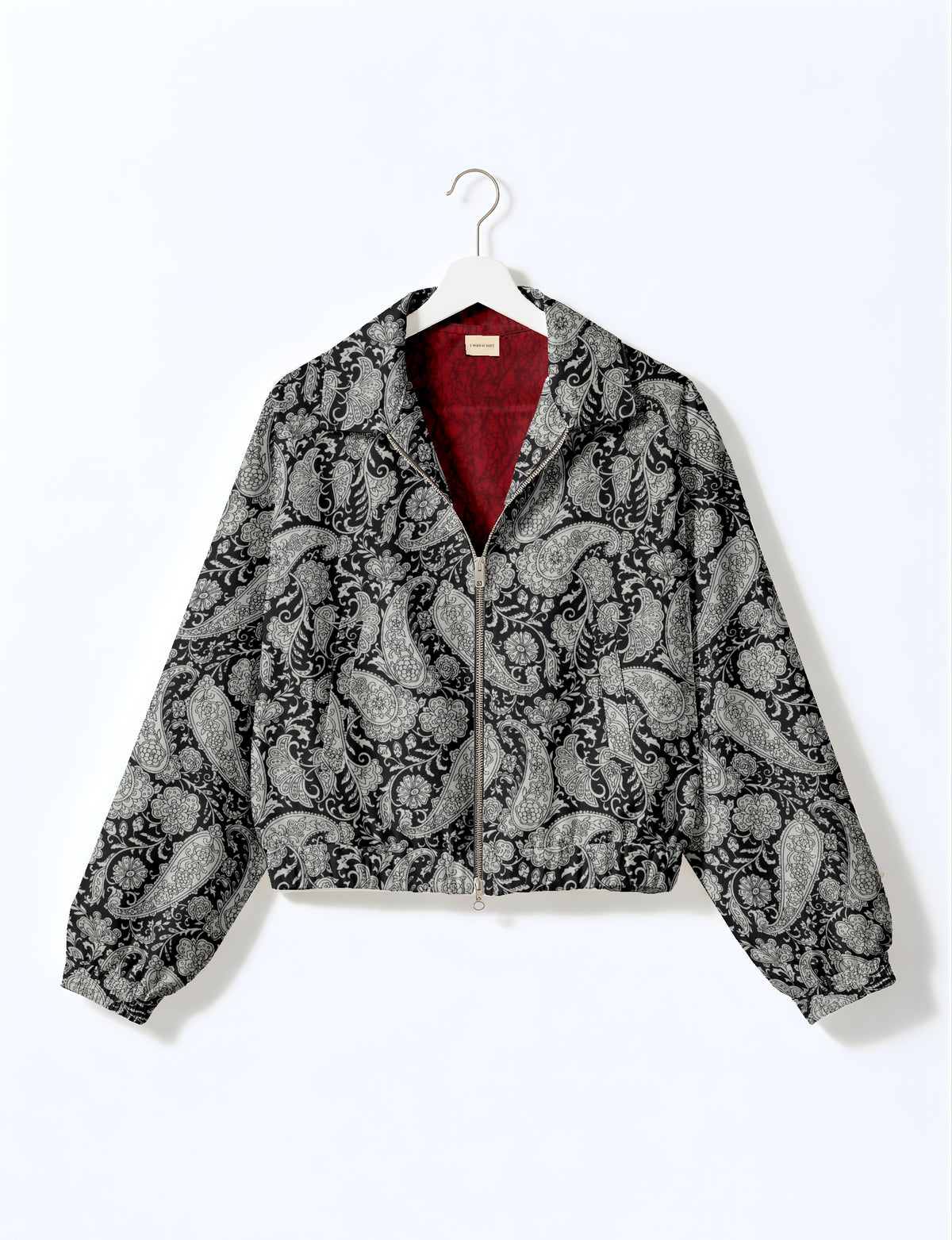 Black bomber jacket with white paisley pattern, front zipper, elastic cuffs and hem, red inner lining, hanging on white