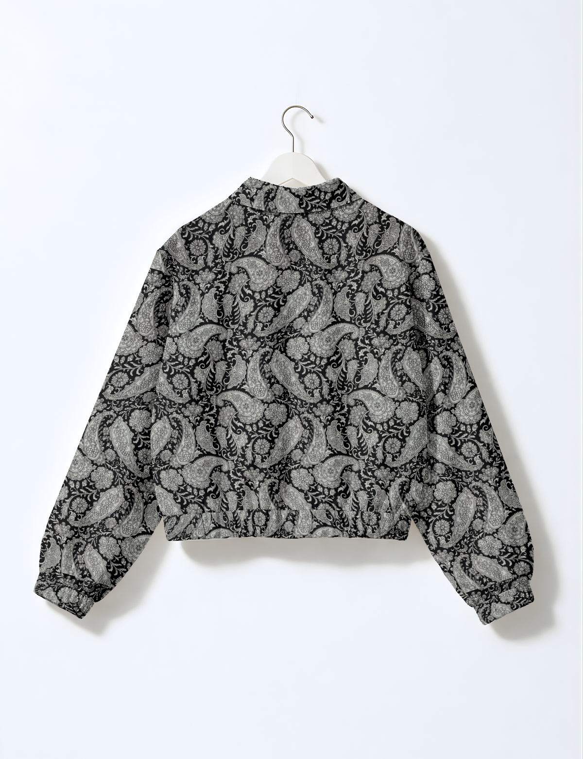 Black bomber jacket with gray paisley and floral pattern, elastic cuffs and waistband, shown from back on white hanger