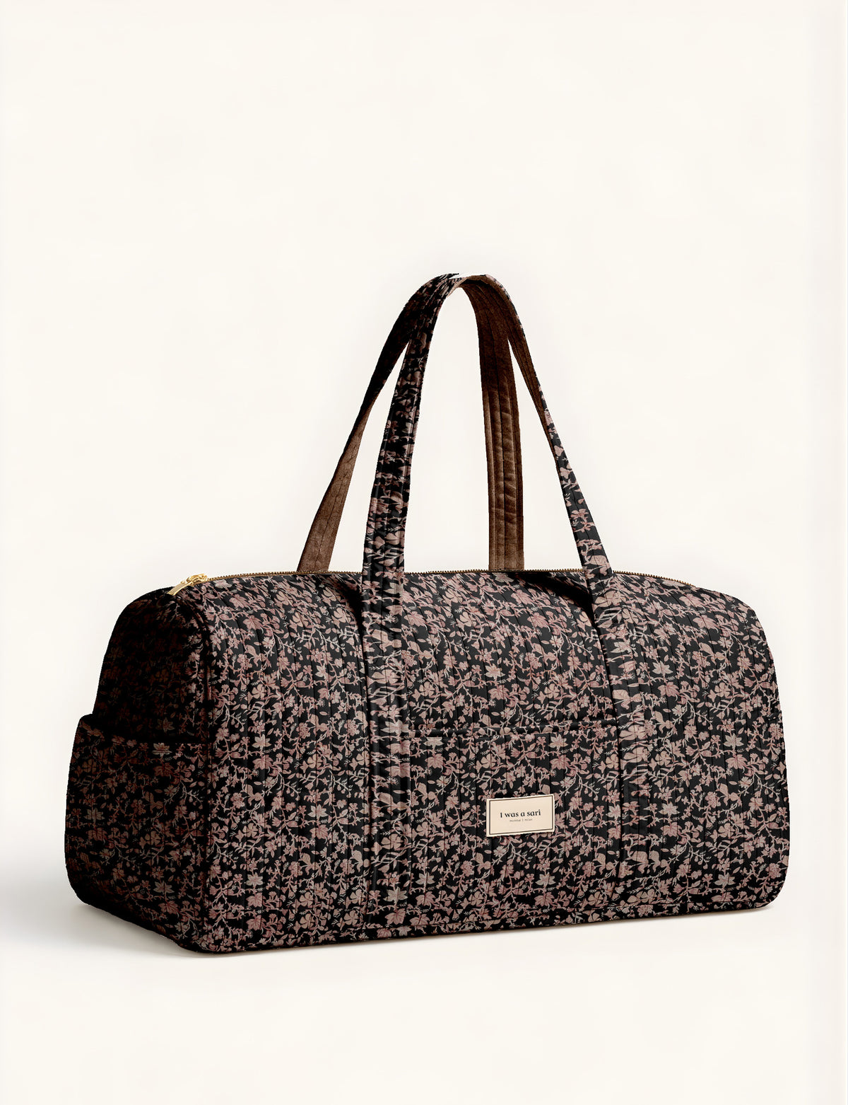 Woman holding a brown paisley quilted barrel bag with front zipper pocket, wearing light blue jeans and white sneakers