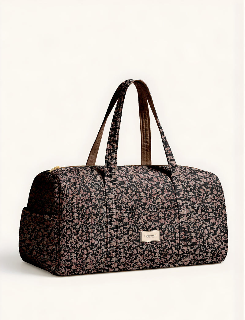 Woman holding a brown paisley quilted barrel bag with front zipper pocket, wearing light blue jeans and white sneakers