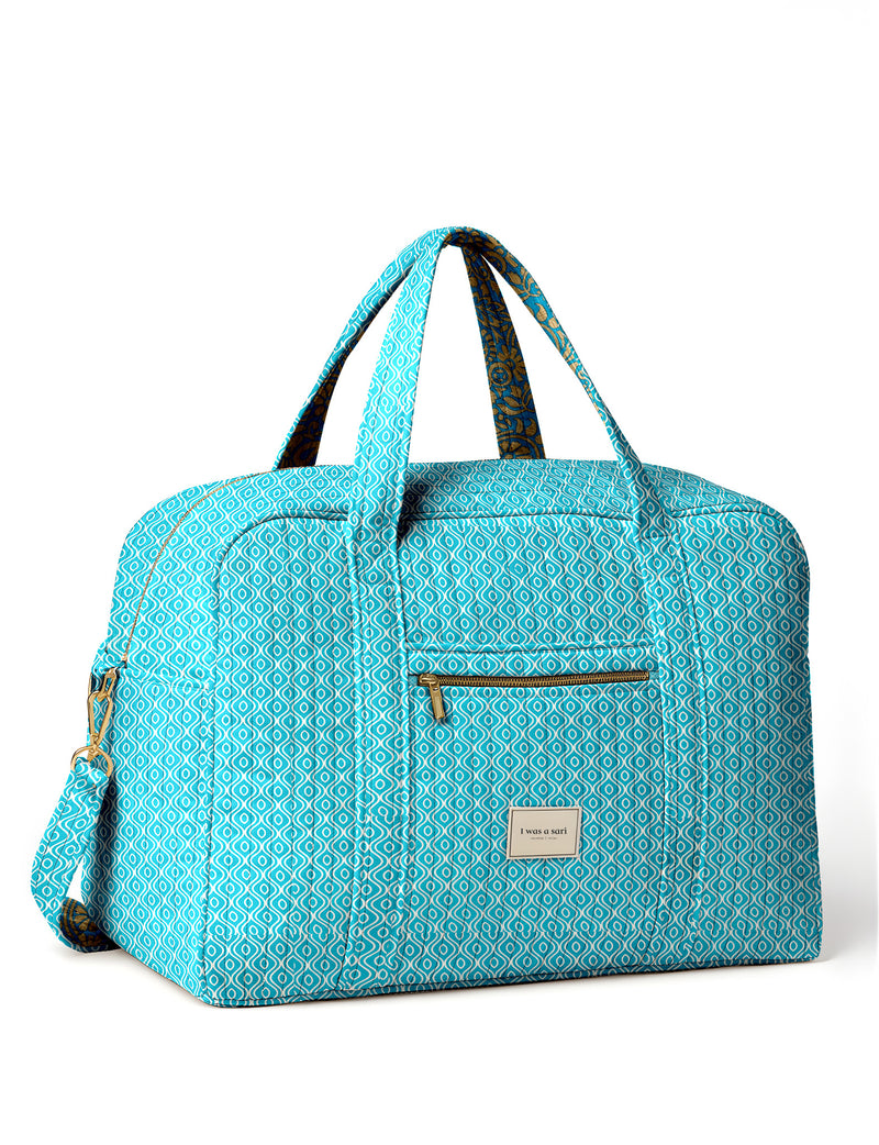 Brown quilted duffle bag with paisley pattern, front zip pocket, dual handles, and label reading "I was a sari"