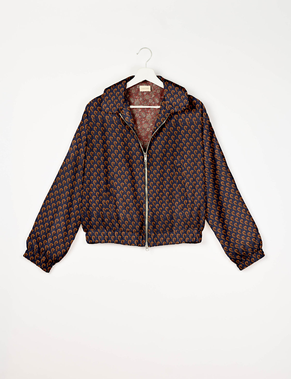 Blue bomber jacket with orange micro pattern, front zipper, elastic cuffs and hem, hanging on white hanger, red paisley