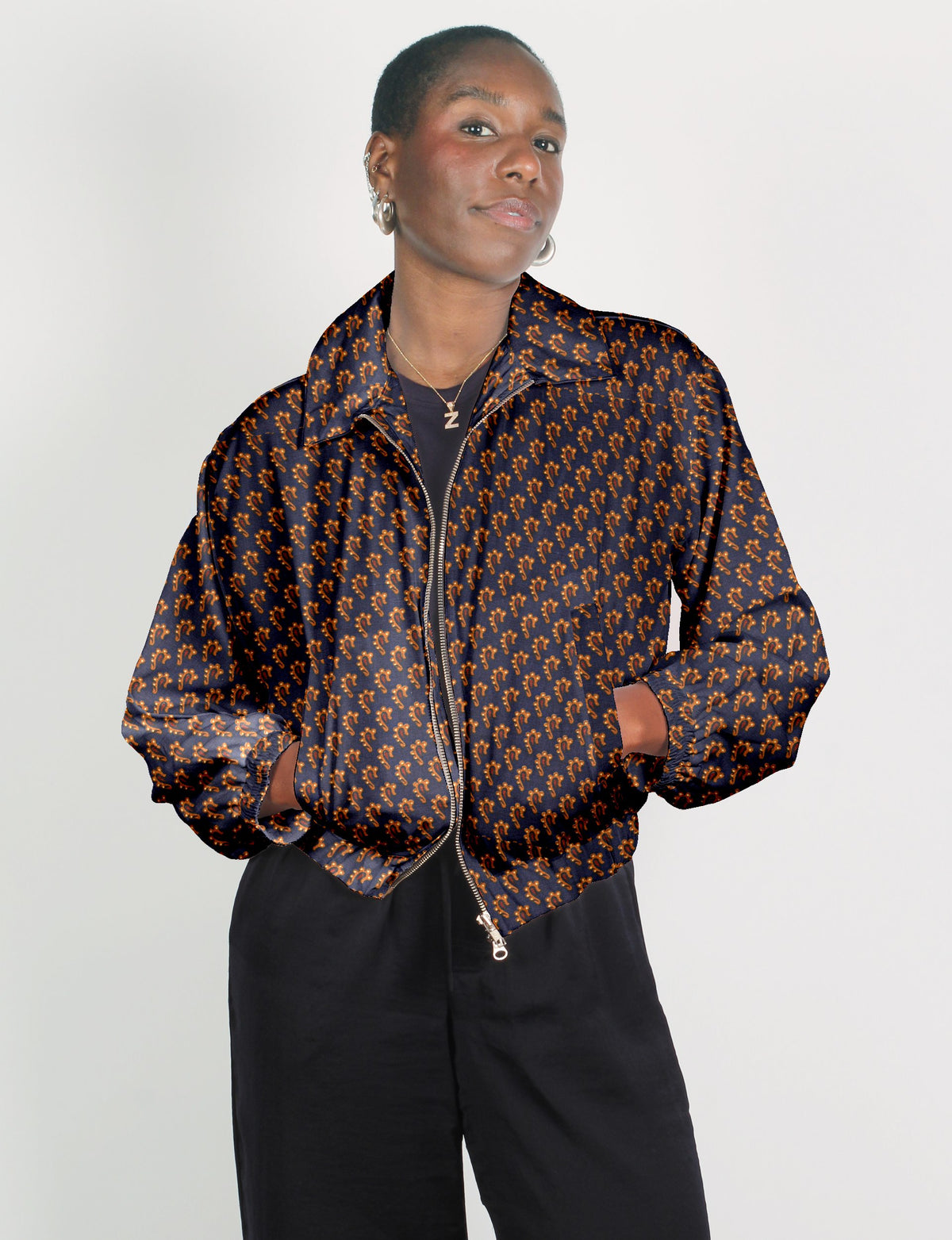 Woman wearing a blue bomber jacket with an orange micro pattern, front zipper, and elastic cuffs, paired with black pants
