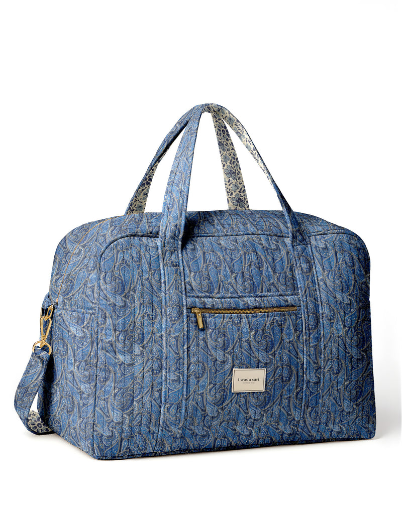 Brown quilted duffle bag with paisley pattern, front zip pocket, dual handles, and label reading "I was a sari"