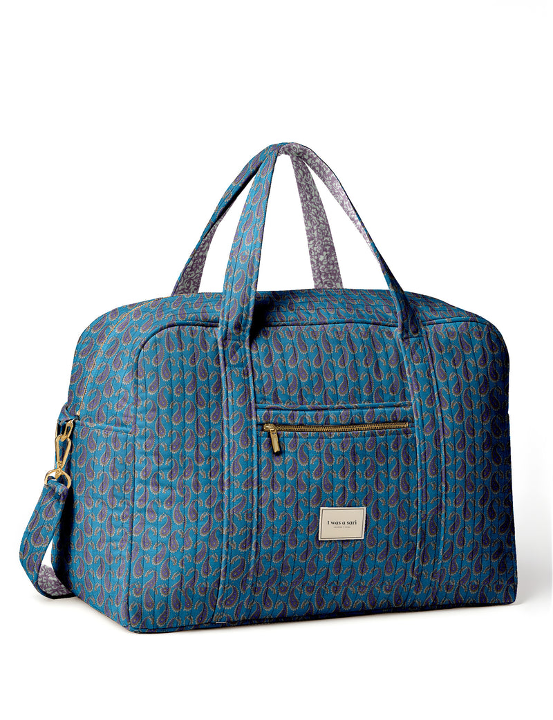 Brown quilted duffle bag with paisley pattern, front zip pocket, dual handles, and label reading "I was a sari"