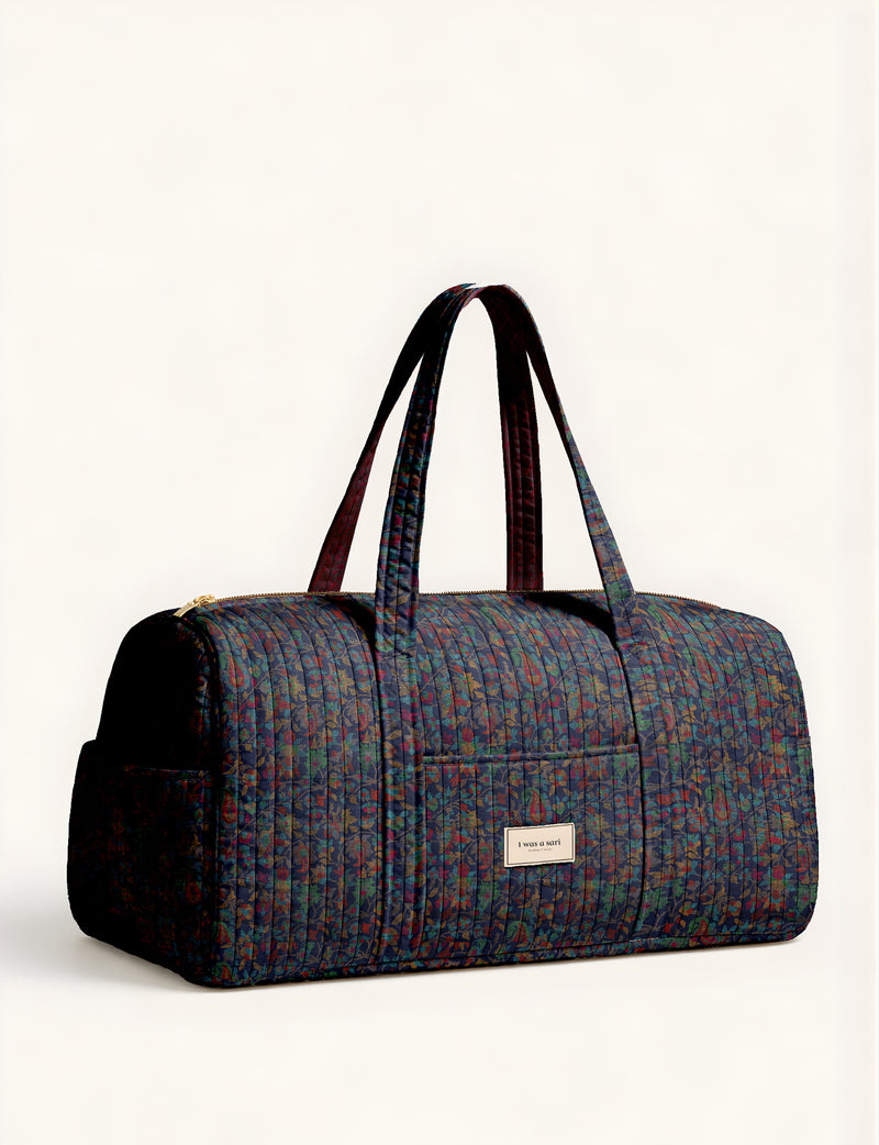 Woman holding a brown paisley quilted barrel bag with front zipper pocket, wearing light blue jeans and white sneakers